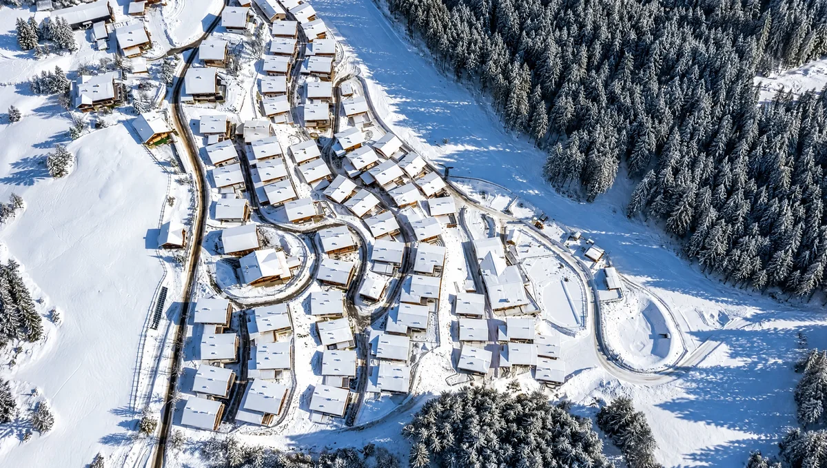 Das Chaletdorf im Winter von oben: freistehende Chalets entlang der Wege, rundherum verschneiter Wald