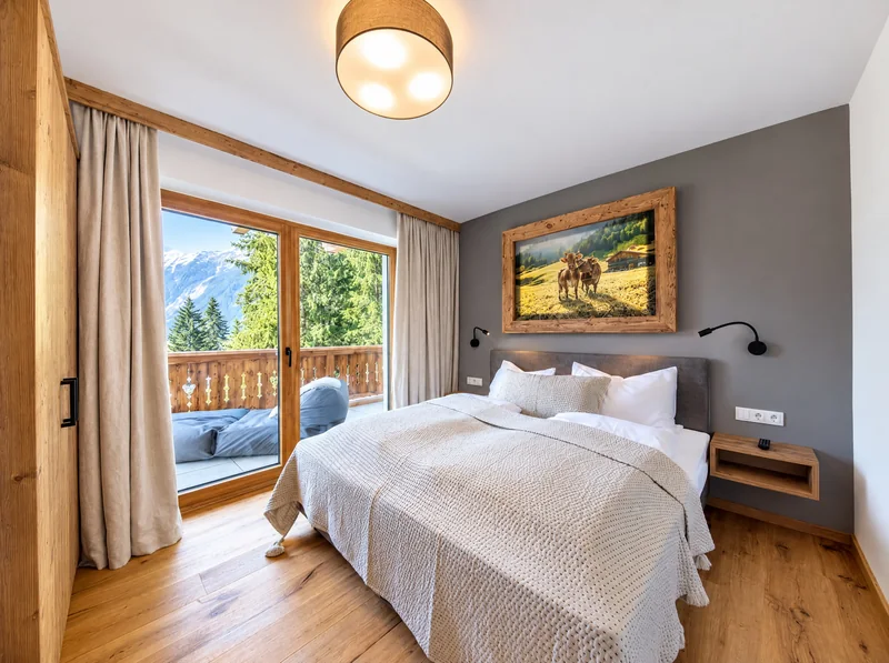 Schlafzimmer mit Doppelbett, Fenstertür zum Balkon und Holzboden